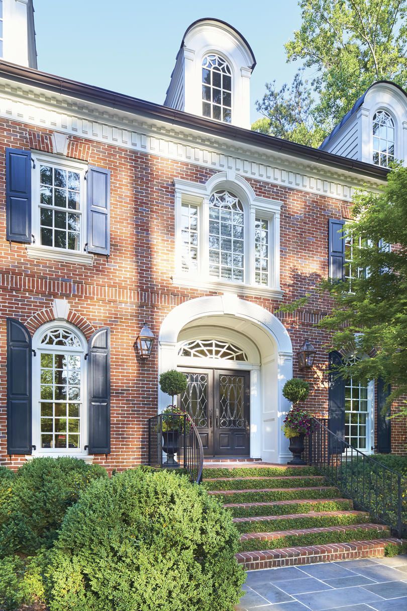 Red brick Georgian estate with white trim, dark shutters, an arched entry and brick steps